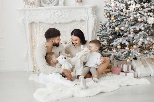 Young family in white clothes sitting near Christmas tree