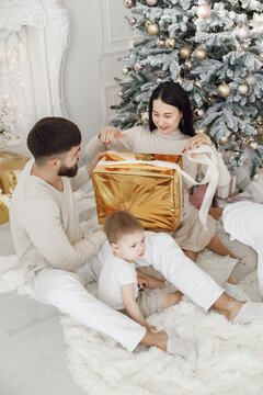 Young family in white clothes sitting near Christmas tree