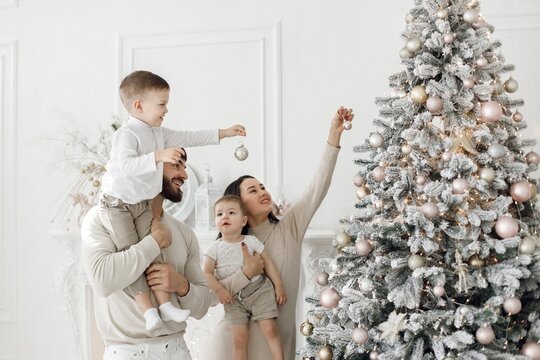 Young family in white clothes decorating the Christmas tree at home