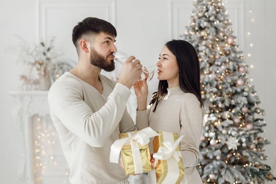 Romantic couple standing near Christmas tree with glasses of champagne