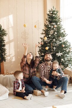 Young family in plaid shirts sitting near Christmas tree