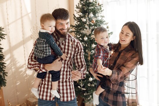 Young family in plaid shirts standing near Christmas tree with a sparklers