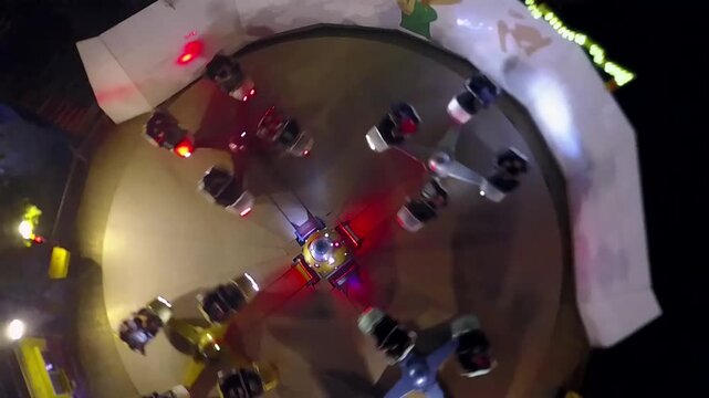 Top-down drone shot of a whirling cup ride with riders at a night funfair, Mosul, Iraq