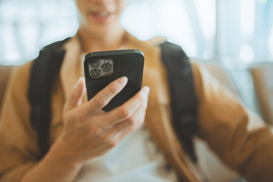 Close up of young traveler holding smartphone while wearing backpack, using mobile technology during journey.