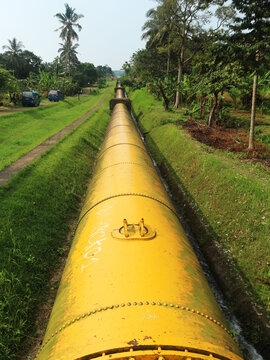 A long yellow penstock pipe stretches approximately 1.5 kilometers as part of a hydroelectric power generation system in Bogor, West Java, Indonesia. The bright yellow pipe stands out vividly.