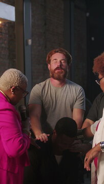 Diverse church members laying hands in supportive prayer over a man during indoor worship service for spiritual healing and blessings