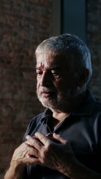 Senior elderly man placing hands over heart with deep emotional devotion and sorrow during indoor church worship service for healing
