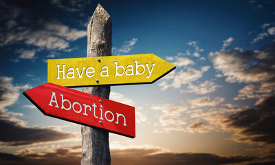 Have a baby or abortion - wooden signpost with two arrows, sunset sky in background © PX Media