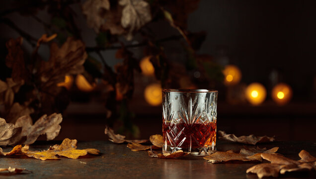 Whisky crystal glass on the table amidst dried oak leaves.