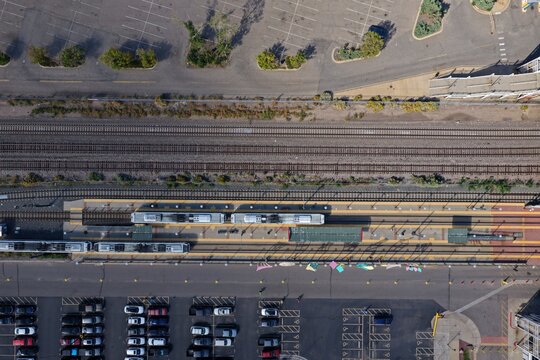 Aerial view of a light rail station with trains stopped at the platform, adjacent to railway tracks and a large parking lot in Denver, Colorado, United States.