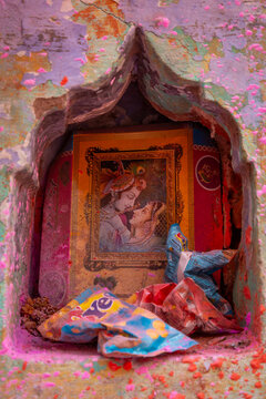 Wall niche with a framed picture of Radha and Krishna covered in colored powder and snack wrappers, Barsana, India
