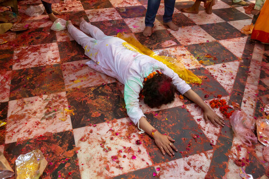 Person lying prostrate in prayer on a checkered floor strewn with petals during Lathmar Holi, Barsana, India