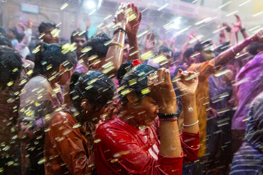 Person in red shirt covering the head under water spray at Holi celebrations in Shri Banke Bihari Temple, Vrindavan, India