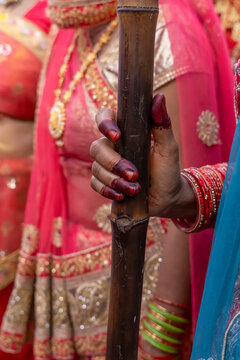 Close up of a hand gripping a bamboo stick with red nail polish beside a pink sari at Lathmar Holi, Barsana, India