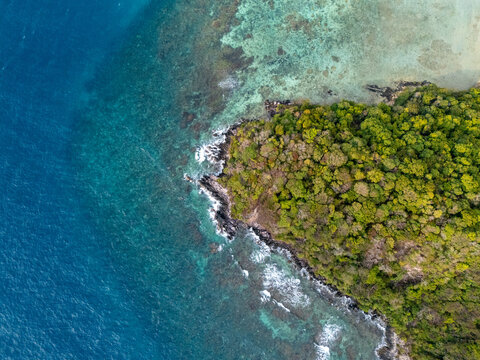 Aerial view of Karimun Jawa island showing lush green tropical forest meeting the turquoise coral reef and deep blue sea in Karimunjawa, Central Java, Indonesia.