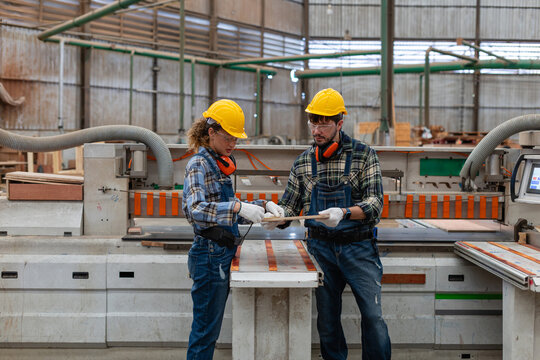 A carpenter inspects plywood for woodworking alongside a woman and two colleagues in a wood workshop beside a panel saw.