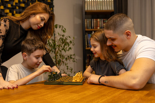 Aunt and uncle playing chess with nephew and niece at home