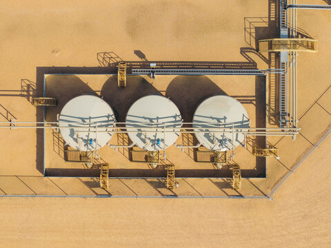 Aerial view of three large circular storage tanks at a natural gas processing facility with industrial piping and infrastructure in Brighton, Colorado, United States.