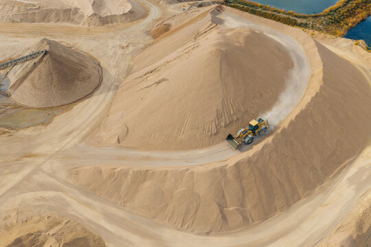 Aerial view of a wheel loader operating on a large sand and gravel pile at an open-pit quarry with conveyor systems and earthmoving tracks in Brighton, Colorado, United States.
