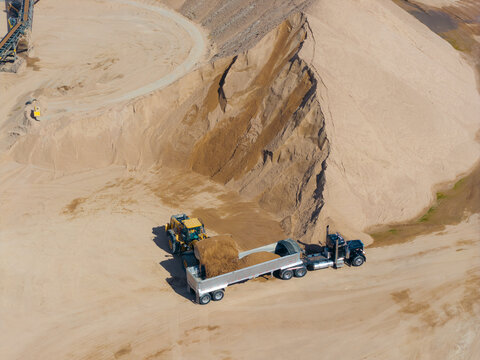 Aerial view of a sand and gravel quarry with a front-end loader filling a dump truck near large piles of aggregate in Brighton, Colorado, United States.