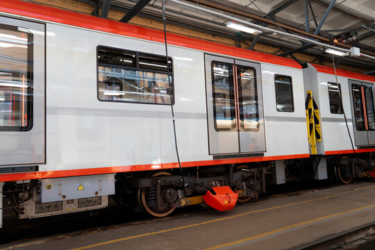 Side view of a modern white passenger train with orange trim inside a maintenance workshop, featuring passenger doors, windows, wheels, suspension and technical equipment.