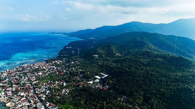 Aerial view of Karimunjawa town nestled between lush green mountains and the turquoise waters of the Java Sea in Karimunjawa, Central Java, Indonesia.