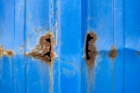 Rusty holes on a blue corrugated metal surface. This detailed texture is ideal for industrial design, architectural backgrounds, and themes of decay or urban weathering.