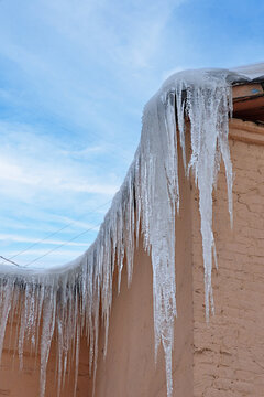 Icicles and large layer Ice hanging from roof against blue sky. Winter landscape
