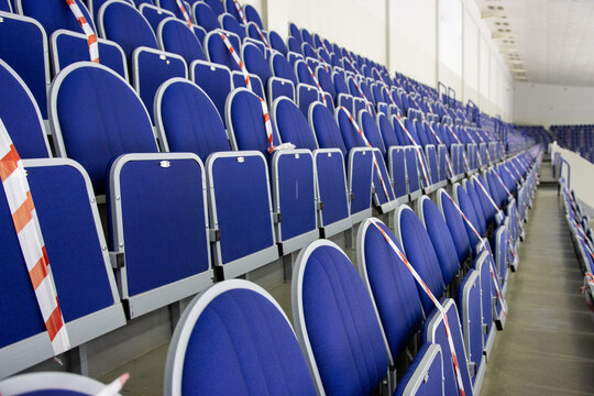 Empty blue seats arranged in rows with safety tape in a sports arena
