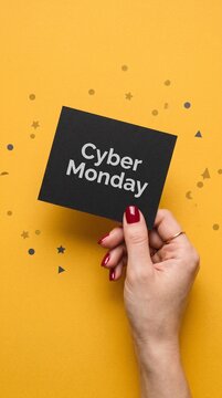 A hand holds a black card with Cyber Monday written in white on a bright yellow background with confetti