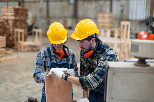 Plywood for woodworking: a carpenter and her male colleague inspect a wood piece beside wooden pallets in a wood workshop.