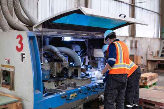 The machine receives maintenance as a technician and his male colleague inspect the open moulder beside stacked lumber.