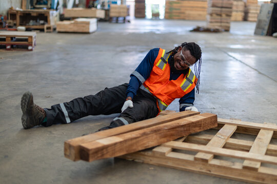 Lumber, following workplace accident injury, lies beside a seated man clutching his knee in pain near a wooden pallet.