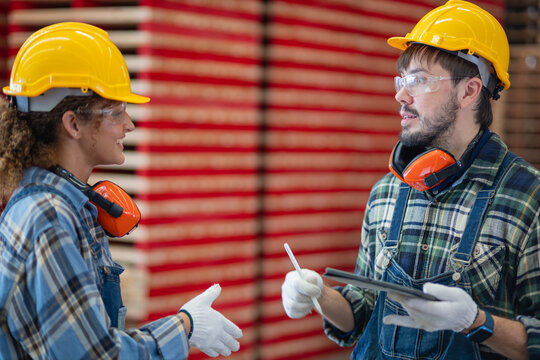 During carpentry workshop discussions, a woman working as a female carpenter consults her male colleague holding a tablet.