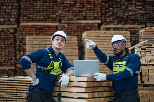 Team meeting: teamwork among factory workers is evident as two men look away beside a laptop resting on stacked lumber.