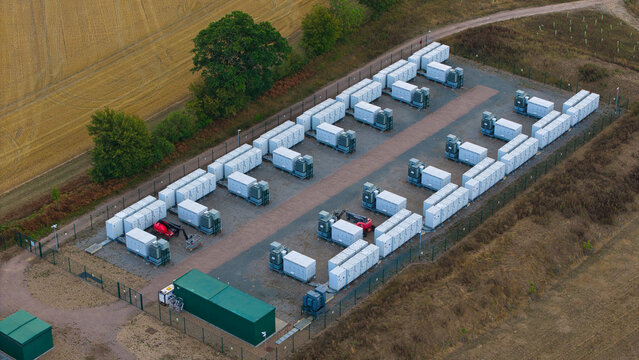 Aerial view of Bramford Substation Battery Energy Storage facility featuring rows of white energy storage units and cooling systems within a fenced compound in Bramford, England, United Kingdom.