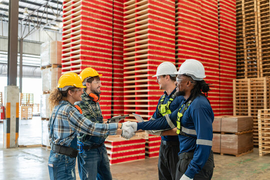 Demonstrating teamwork, four factory workers attend a team meeting as two shake hands beside colleagues holding a laptop and tablet.