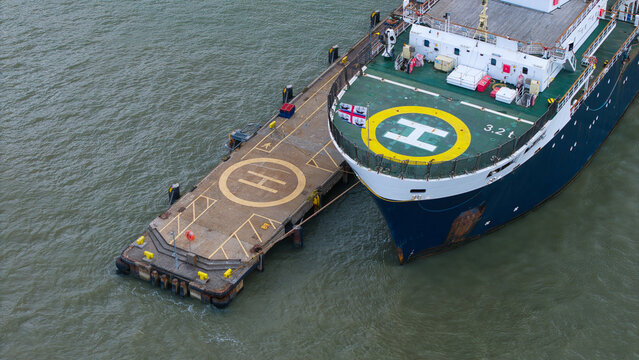 Aerial view of a Trinity House lighthouse tender vessel docked at a pier with helipads on both the ship deck and the concrete jetty in Harwich, England, United Kingdom.