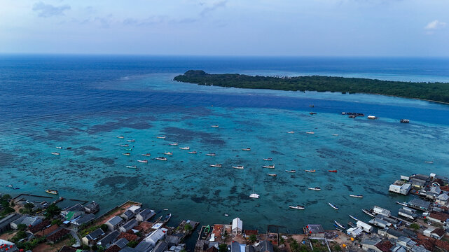 Aerial view of Karimunjawa featuring a turquoise lagoon with numerous small fishing boats, coral reefs, and a coastal village in Karimunjawa, Central Java, Indonesia.