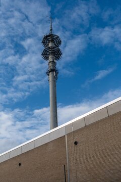 Tall communication tower near building under blue sky with clouds