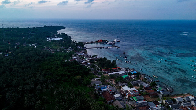 Aerial view of Port Karimunjawa with boats docked at the pier, coastal buildings, and turquoise waters in Karimunjawa, Central Java, Indonesia.