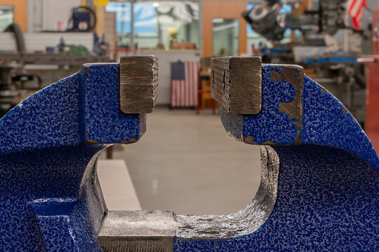 Industrial workroom with blue vise in the foreground and american flag in the background appearing to be squeezed.