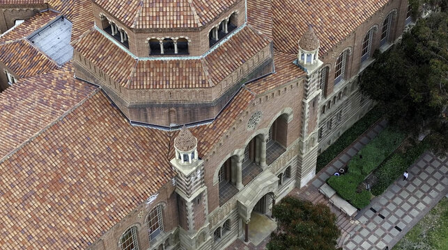 Aerial view of Royce Hall at UCLA Campus, featuring Romanesque Revival architecture, red-tiled roof, and arched windows, surrounded by walkways and greenery in Westwood, California, United States.