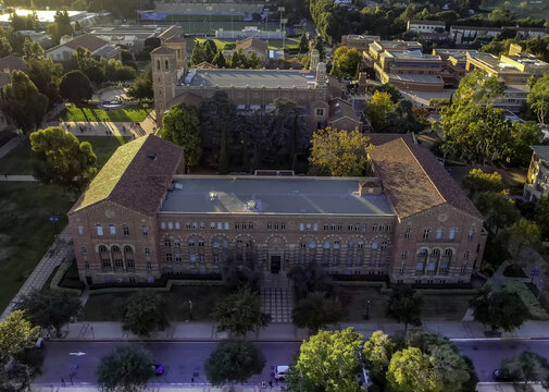 Aerial view of the historic Royce Hall at the UCLA Campus, featuring its iconic twin towers, red-tiled roofs, and surrounding lush greenery in Westwood, California, United States.