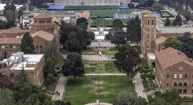 Aerial view of the UCLA campus in Westwood, featuring historic red-brick buildings, lush green lawns, walkways, and trees under an overcast sky. Westwood, California, United States.