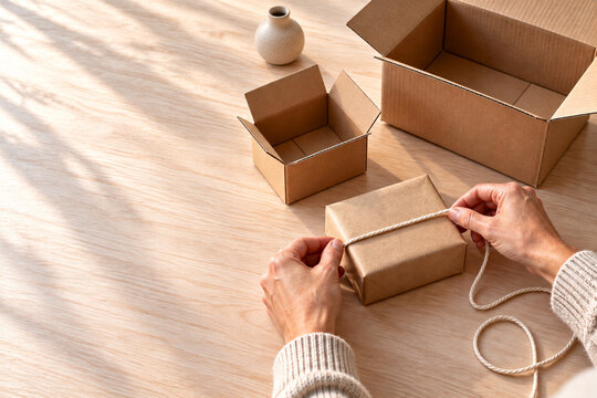 Woman wrapping a small gift box with string on a wooden table  