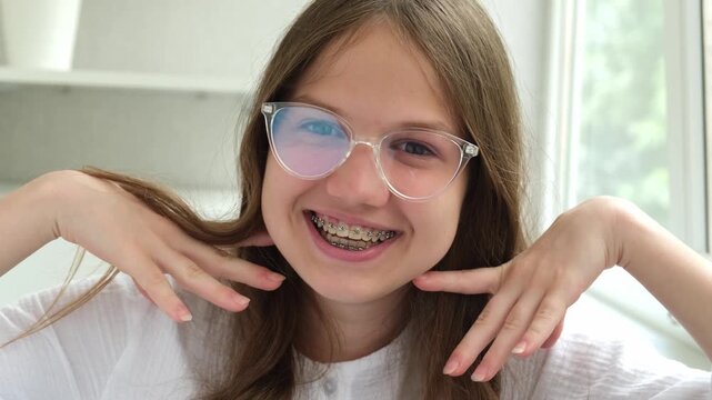 Funny happy teen girl in glasses with braces smiling showing teeth. Orthodontic treatment for adolescents concept