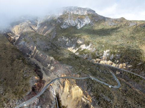 Aerial view of the winding road traversing the rugged volcanic landscape of Nevado del Ruiz, with steep rocky slopes and mist-covered peaks, Villamaria, Caldas, Colombia.