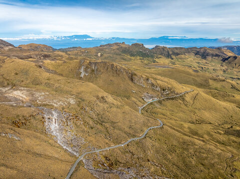 Aerial view of the Nevado del Ruiz volcano landscape with a winding mountain road cutting through rugged, golden-brown Andean terrain in Villamaria, Caldas, Colombia.