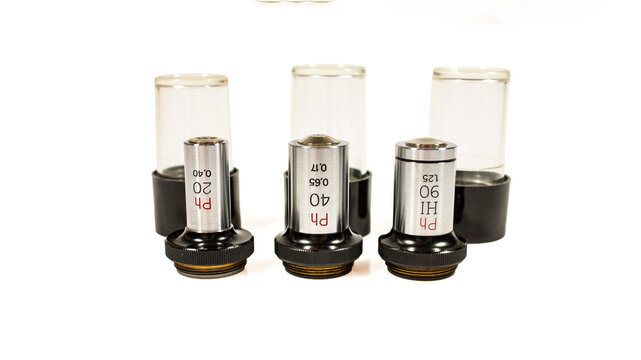 Set of three phase contrast microscope objectives with 20x, 40x and 90x magnification, silver metal barrels, black mounting rings and transparent protective caps, isolated on a white background.